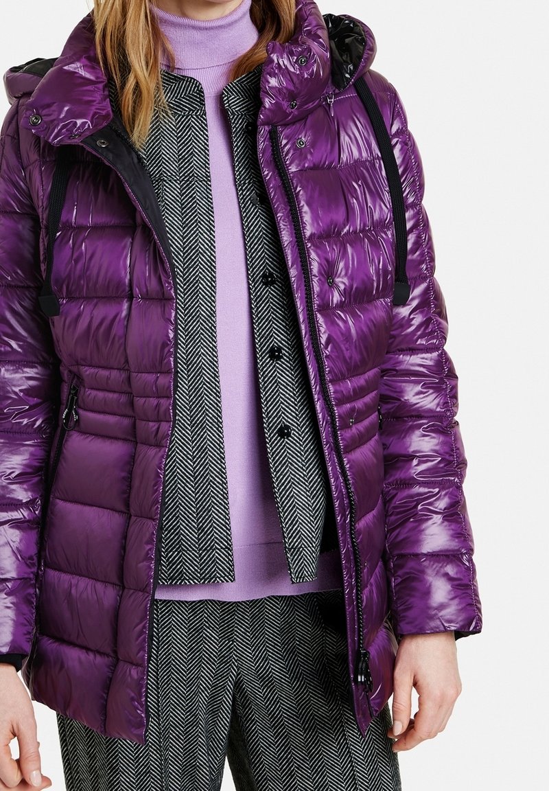 Lila puffjacka med en blank yta, med huva, dragkedja och justerbara remmar. Bärs över en lavendeltröja och houndstooth-byxor.