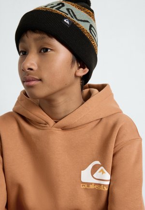 Sweatshirt à capuche marron avec un logo blanc et jaune sur le devant. Porté avec un bonnet en tricot noir avec des motifs orange et teal.