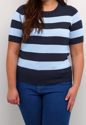 Femme portant un t-shirt à manches courtes rayé horizontalement bleu marine et bleu clair et un jean bleu, debout les bras détendus le long du corps.