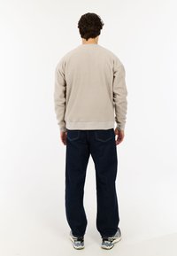 Lichtgrijze fleece sweatshirt met een ronde hals en ribgebreide manchetten, gecombineerd met donkere blauwe wijde jeans en gemusterde sneakers.