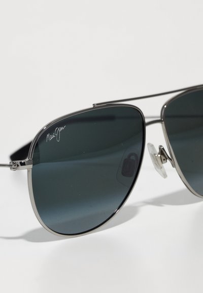 Aviator-aurinkolasit tummilla linsseillä, metallinhohtoinen hopeakehys, allekirjoituslogo linssissä ja läpinäkyvät nenätyynyt. Minimalistinen muotoilu, jossa on sulavalinjaista suunnittelua.