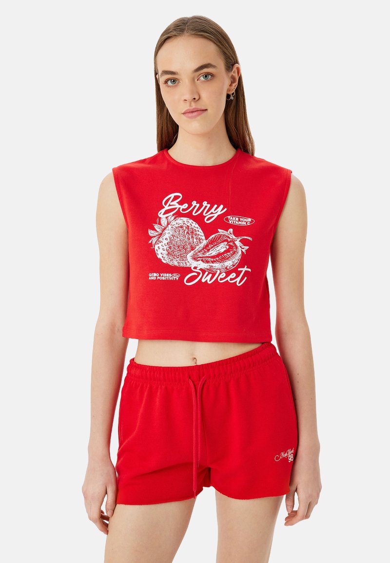 Top corto de algodón rojo con mangas cortas que presenta texto gráfico blanco e ilustraciones de frutas; combinado con pantalones cortos rojos con cordón a juego.