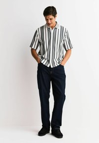 Short-sleeve button-up shirt with black and white vertical stripes, paired with dark blue jeans and black shoes. Casual fit and design.