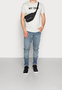Grå t-shirt med svart text "IKVÄLL INTE", slitna blå jeans, svart axelremsväska och svarta sneakers med vita detaljer.