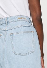 Jeans in denim azzurro chiaro con vita alta, dotati di un logo dorato "GESTUZ" sulla cintura e tasche posteriori standard con dettagli cuciti.
