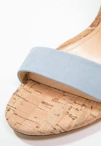 Gros plan sur l'orteil d'une sandale avec une semelle à texture de liège et une large bride en suède bleu clair traversant le pied.
