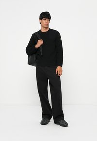 Pulover negru cu un model texturat, guler rotund, asortat cu pantaloni negri largi și adidași negri masivi. O geantă neagră este purtată pe o umăr.