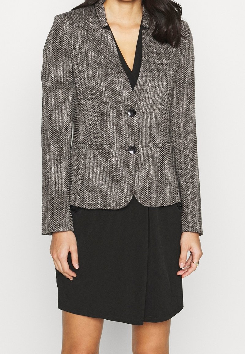 Blazer ajusté en tissu texturé gris et noir avec un motif pied-de-poule, deux boutons et des revers crantés, associé à une robe noire en dessous.