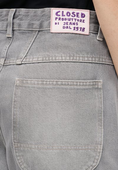 Πίσω τσέπη και μέση ανοιχτόγκρι τζιν με λευκή και μωβ ετικέτα «CLOSED Produttore di Jeans Dal 1978».