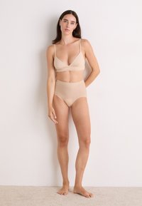 Set de sutien bej și chiloți cu talie înaltă. Țesătură moale, elastică, cu o textură fină. Design simplu, fără modele sau detalii metalice vizibile.