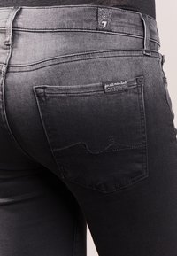 Czarne dżinsy o średnim stanie, z tylnymi kieszeniami ozdobionymi przeszyciami oraz markową metką na pasku. Gładka tekstura.