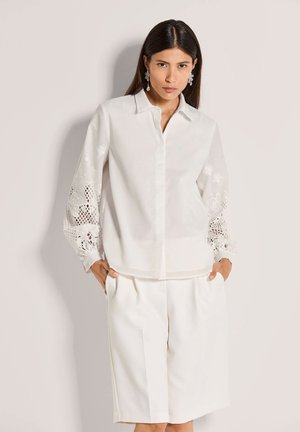 Weißes Hemd mit Knöpfen und Spitzendetails an den langen Ärmeln, kombiniert mit weißen, plissierten Shorts. Glatter Stoff, legere Passform.