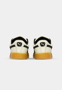 Puma sneakers featuring a cream upper, black accents, and a textured gum sole, with a rounded heel and padded collar for comfort.