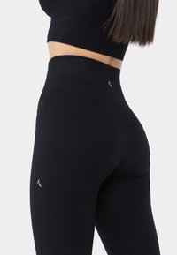 Black high-waisted leggings made of stretchy material, featuring a seamless design and subtle branding on the lower leg.