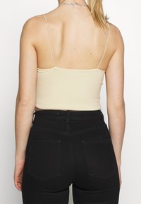 Top corto beige de canalé con tirantes finos tipo espagueti, combinado con jeans negros de talle alto que muestran bolsillos traseros y detalles cosidos.