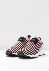 Slip-on idrottsskor med svarta och rosa randiga vävda ovandel, texturerad häl, vit sula och subtil märkeslogotyp på den elastiska remmen.