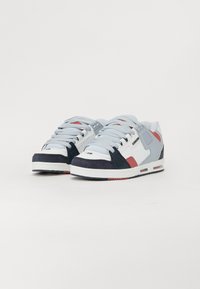 Light blue and white sneakers with red and navy accents, featuring a lace-up design, textured panels, and a visible midsole air cushion.