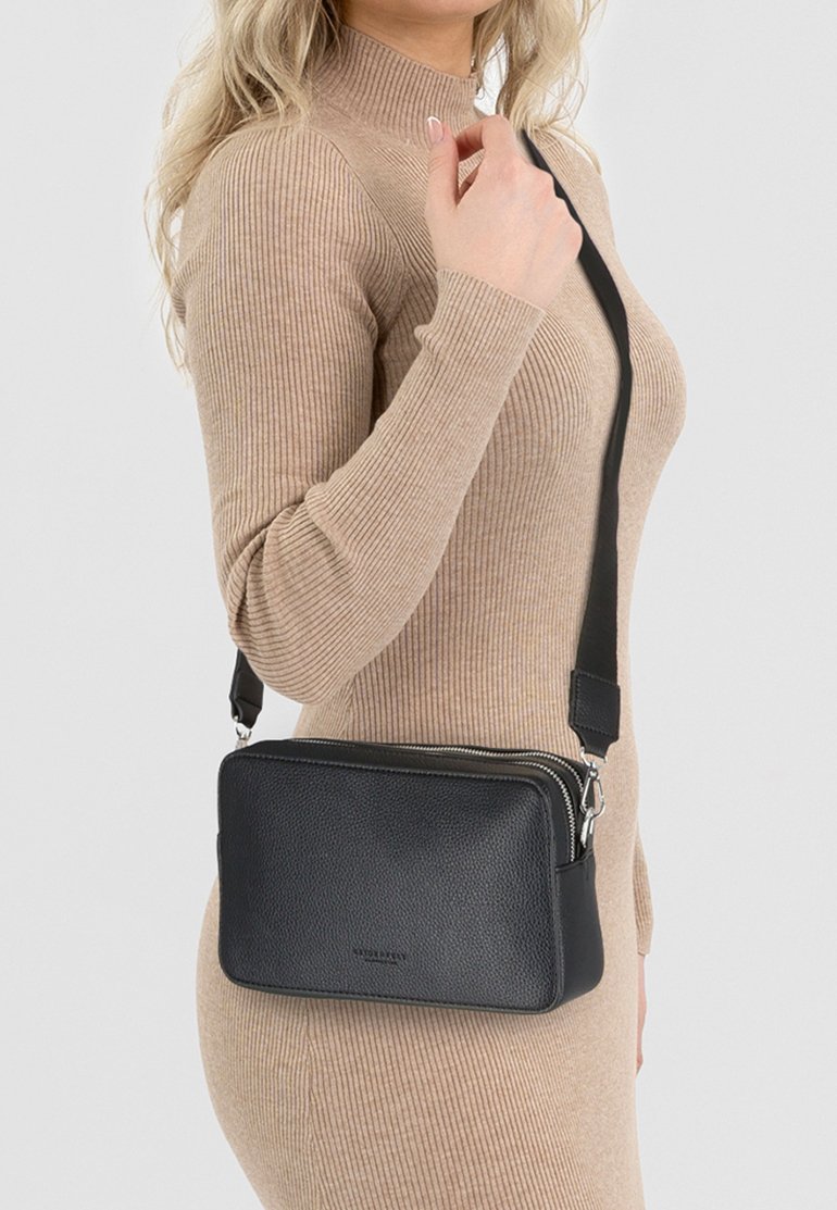 Borsa a tracolla in pelle nera con finitura testurizzata, doppi scomparti con zip e tracolla regolabile, posizionata su uno sfondo neutro.