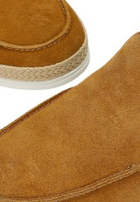 Chaussures à enfiler en daim beige avec bordure en corde tressée autour de la semelle et semelle extérieure en caoutchouc blanc, présentées en gros plan.