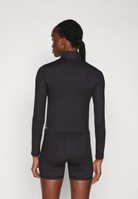 Svart langermet treningsgenser med høy krage, tett design og glatt tekstur. Kombinert med matchende svarte shorts.