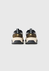 Paire de baskets imprimé animal noir et marron avec semelles beige tachetées, vue de dos sur un fond gris.