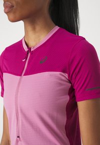 Camiseta deportiva de manga corta en diferentes tonos de rosa, con un tejido texturizado, cierre de cremallera y un logo sutil en el pecho.