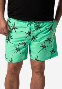 Ljust gröna badshorts med ett svart palmträdsmönster, elastisk midja med dragsko och en slät, glänsande textur.