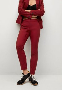 Pantalons taillés bordeaux avec une coupe slim, texture lisse et taille mi-haute, associés à des baskets de sport noires avec des lacets blancs.