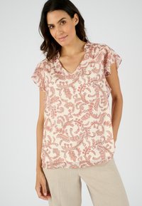 Bloes met bloemenprint in blush pink met rode accenten. Heeft een V-hals en korte fladdermouwen, gemaakt van lichtgewicht stof.