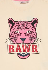 Testa di leopardo rosa con macchie nere e baffi che morde un cartello bianco su cui è scritto "RAWR" in lettere rosse glitterate su tessuto beige.