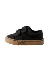 Melnas audekla kurpes ar divām Velcro siksnām, brūnas gumijas zolītes un smaidīga sejas logotips sānos. Apaļa purngala daļa un teksturēta augšdaļa.