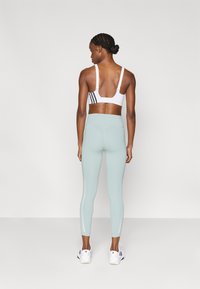 Λευκό αθλητικό σουτιέν με μαύρες ρίγες, σε συνδυασμό με ελαφρώς πράσινο ανοιχτό κολάν. Το κολάν έχει λεία υφή και διακριτικές πλευρικές λεπτομέρειες.