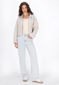 Giacca cropped grigio chiaro con colletto e due tasche frontali, abbinata a jeans a gamba larga in denim chiaro e sneakers bianche con suola beige.