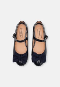 Para czarnych lakierowanych butów Mary Jane z granatowymi materiałowymi kokardkami i paskami na kostkach, beżowymi wkładkami oraz metką marki wewnątrz.