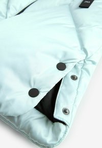 Giacca a vento azzurra chiara con una texture liscia, caratterizzata da bottoni neri e una fodera interna nera. Nota per il suo design trapuntato.
