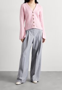 Rosa fluffig kardiagan med V-ringning, prydd med sex runda knappar. Kombinerad med ljusgrå veckade vida byxor och vita spetsiga skor.