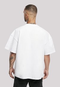Hvit oversized t-skjorte med senkede skuldre, rund hals og korte ermer. Laget av bomull, med en ensfarget tekstur uten mønstre.