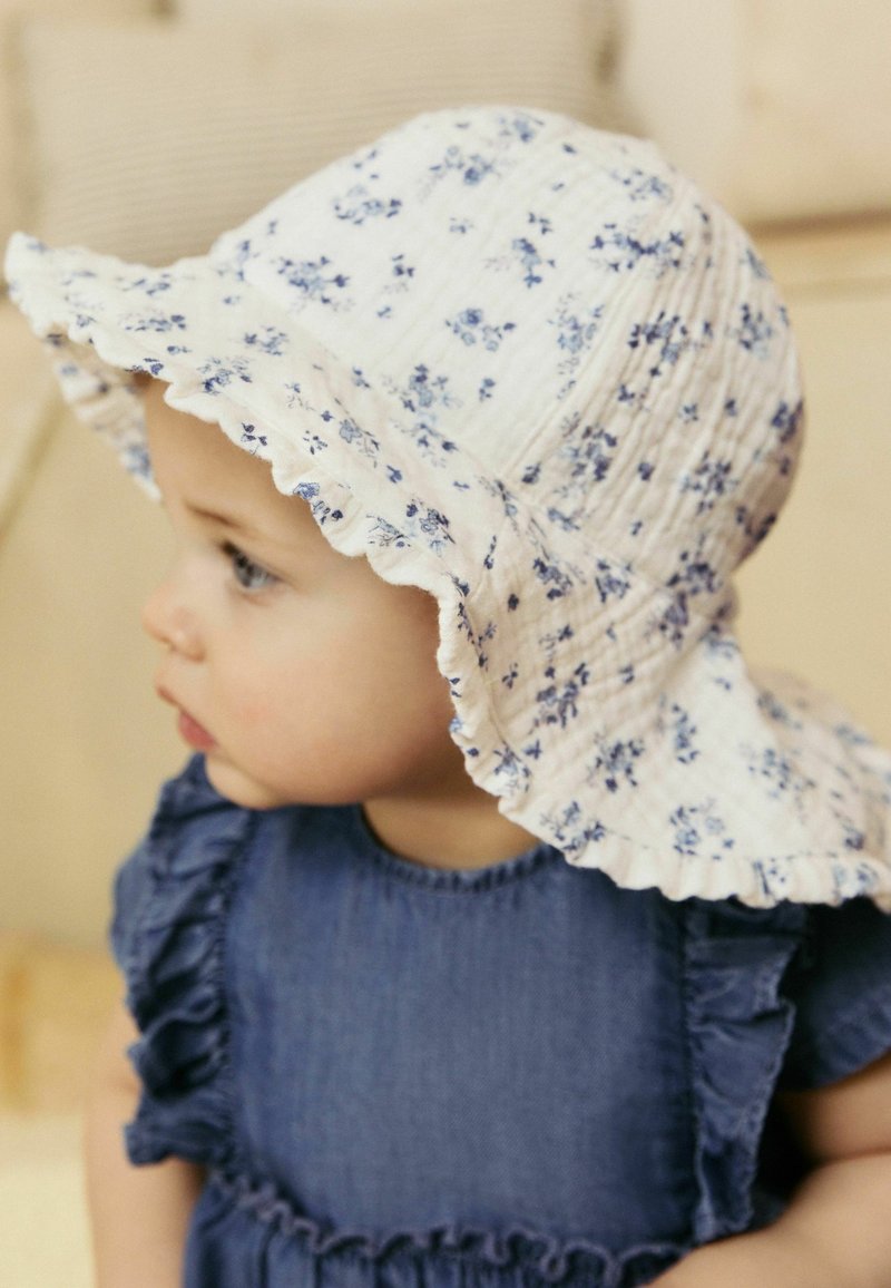 Blumiger Sonnenhut mit rüschigem Rand in Weiß und Blau, aus weichem Stoff gefertigt, getragen mit einem dunkelblauen Kleid mit Rüschensleeves.