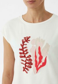 Witte t-shirt met korte mouwen, voorzien van rode en roze koraalontwerpen met pailletten en borduurwerk. Soepele stof met een ronde halslijn.