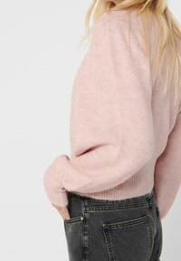 Rosa, stickad tröja med bred halsringning och ballongsärmar, tillsammans med högmidjade svarta jeans. Mjuk, texturerad tyg.