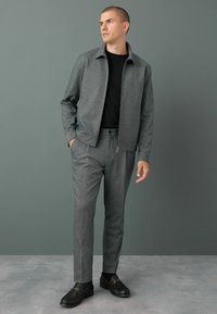 Chaqueta texturizada gris sobre una camiseta negra, combinada con pantalones grises a juego. El conjunto presenta un corte relajado y mocasines negros.