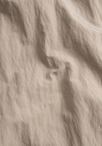 Tessuto beige chiaro con una superficie stropicciata, che mostra un aspetto morbido e naturale e motivi irregolari su tutto il materiale.