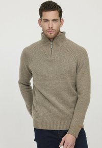 Pull en beige à col montant fabriqué en maille douce, avec une demi-fermeture éclair, des poignets côtelés et des détails sur les côtés.