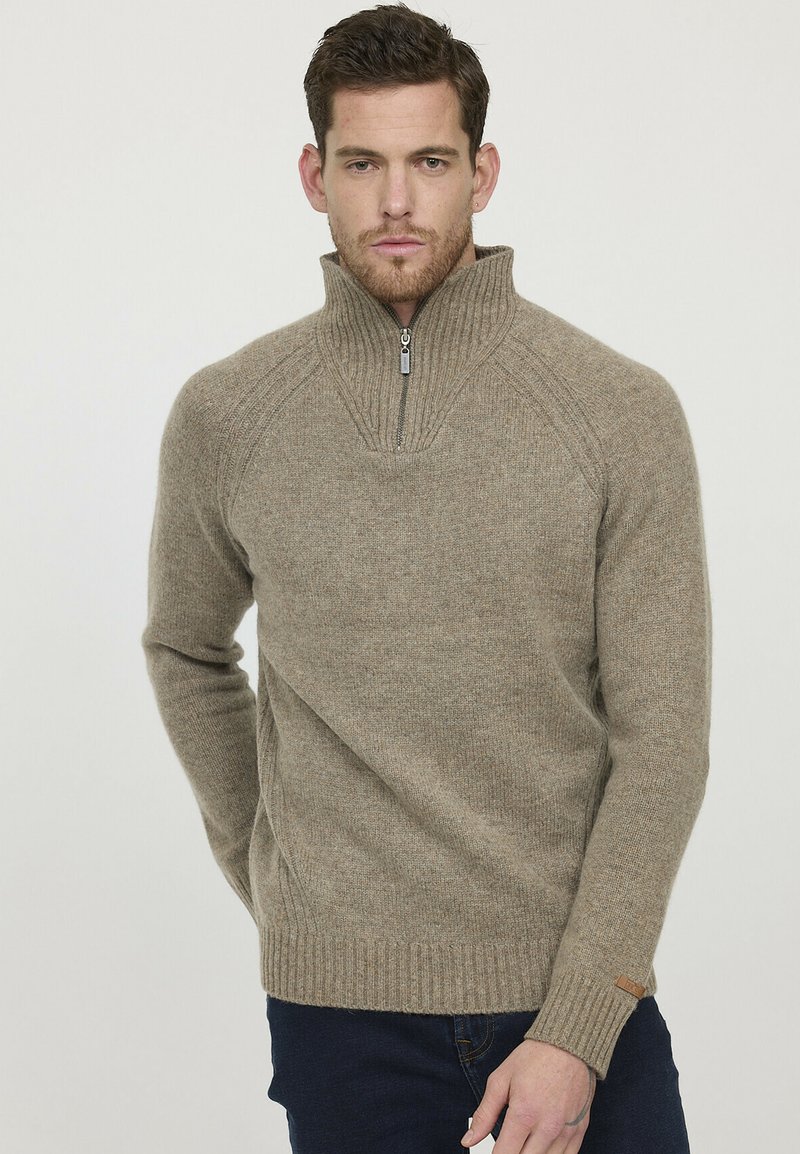 Pull en beige à col montant fabriqué en maille douce, avec une demi-fermeture éclair, des poignets côtelés et des détails sur les côtés.