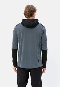 Maglietta a maniche lunghe con cappuccio grigio e dettagli neri, dotata di tasca con zip sul lato e maniche a costine, realizzata in un materiale leggero.