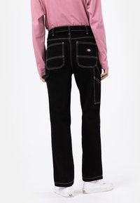 Black corduroy pants with white stitching. Features two back pockets and a side pocket. Worn with a pink long-sleeve top and white shoes.