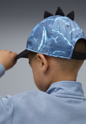 Blaue Kappe mit Blitzmuster, schwarzer Krempe und drei schwarzen Spitzen hinten. Kinderhand richtet die Kappe gerade, während das Kind einen blauen Pullover trägt.