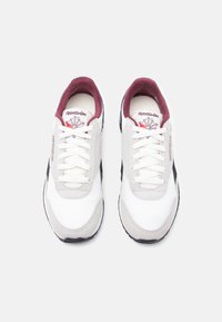 Par bijelih Reebok tenisica s naglascima od sive kože, crnim bočnim trakama i maroon unutrašnjim oblogom, prikazane odozgo na bijeloj pozadini.
