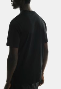Black short-sleeve t-shirt with a classic crew neck, smooth fabric, and a relaxed fit, viewed from the back against a light background.