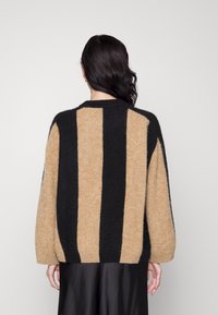 Beige und schwarz gestreifter Pullover mit lockerer Passform, rundem Ausschnitt und weichem Material. Mit auffälligen vertikalen Streifen und heruntergezogenen Schultern.